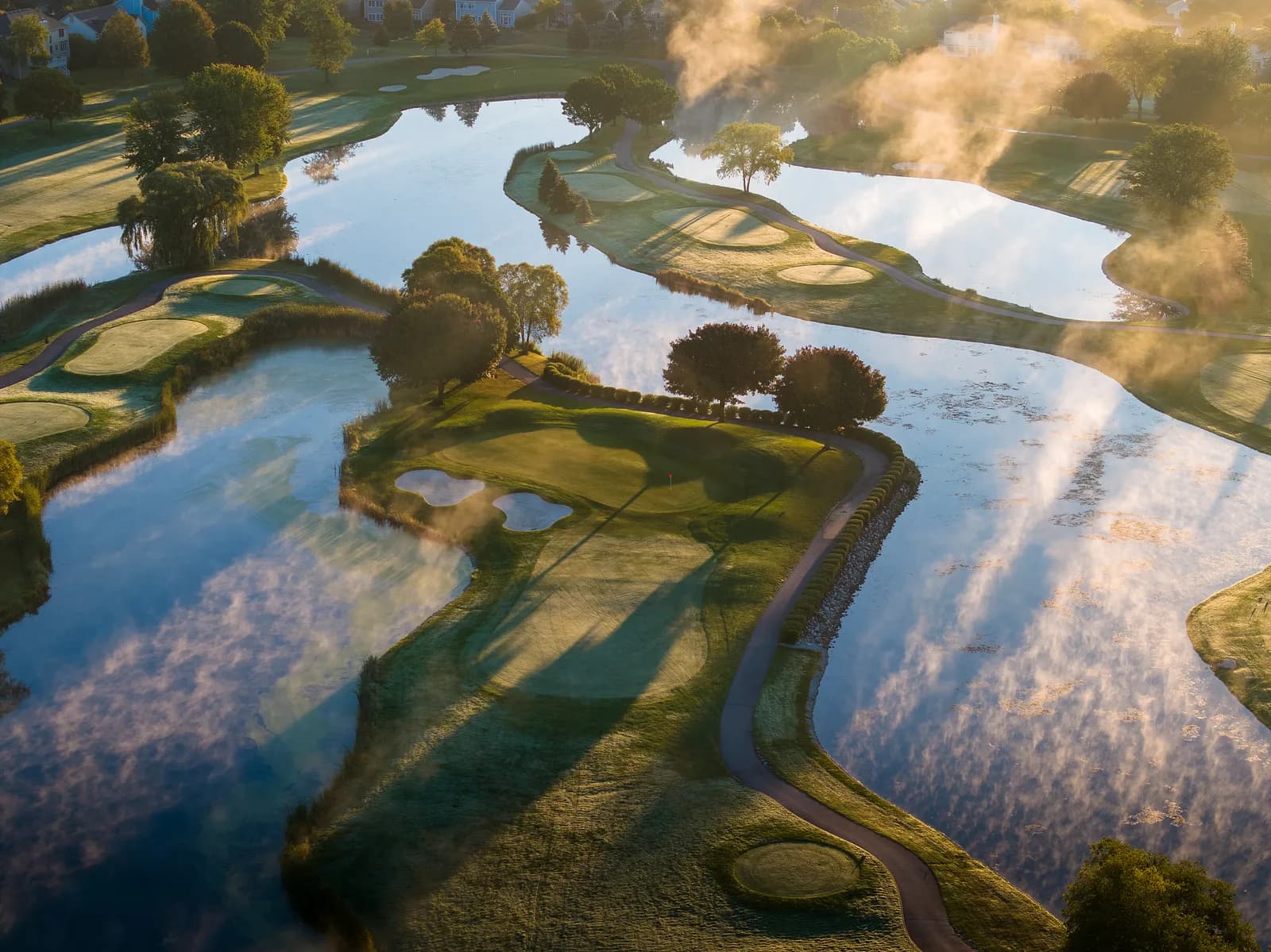Morning mist and cloud reflections drifting across a water-woven course at sunrise