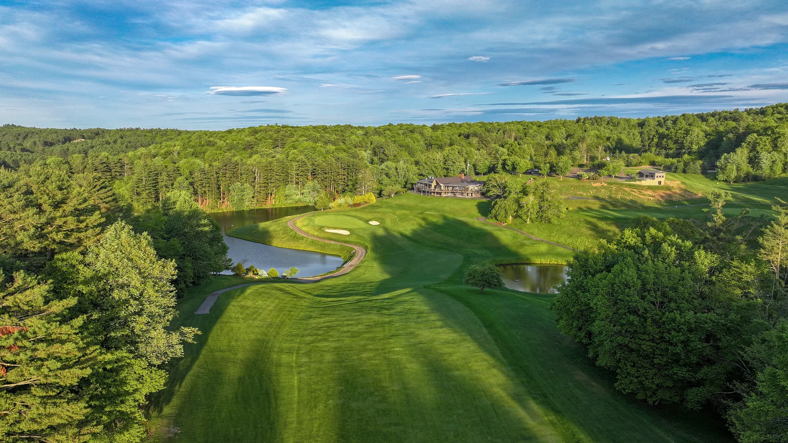 Forest-lined fairway rising toward the clubhouse under a summer sky