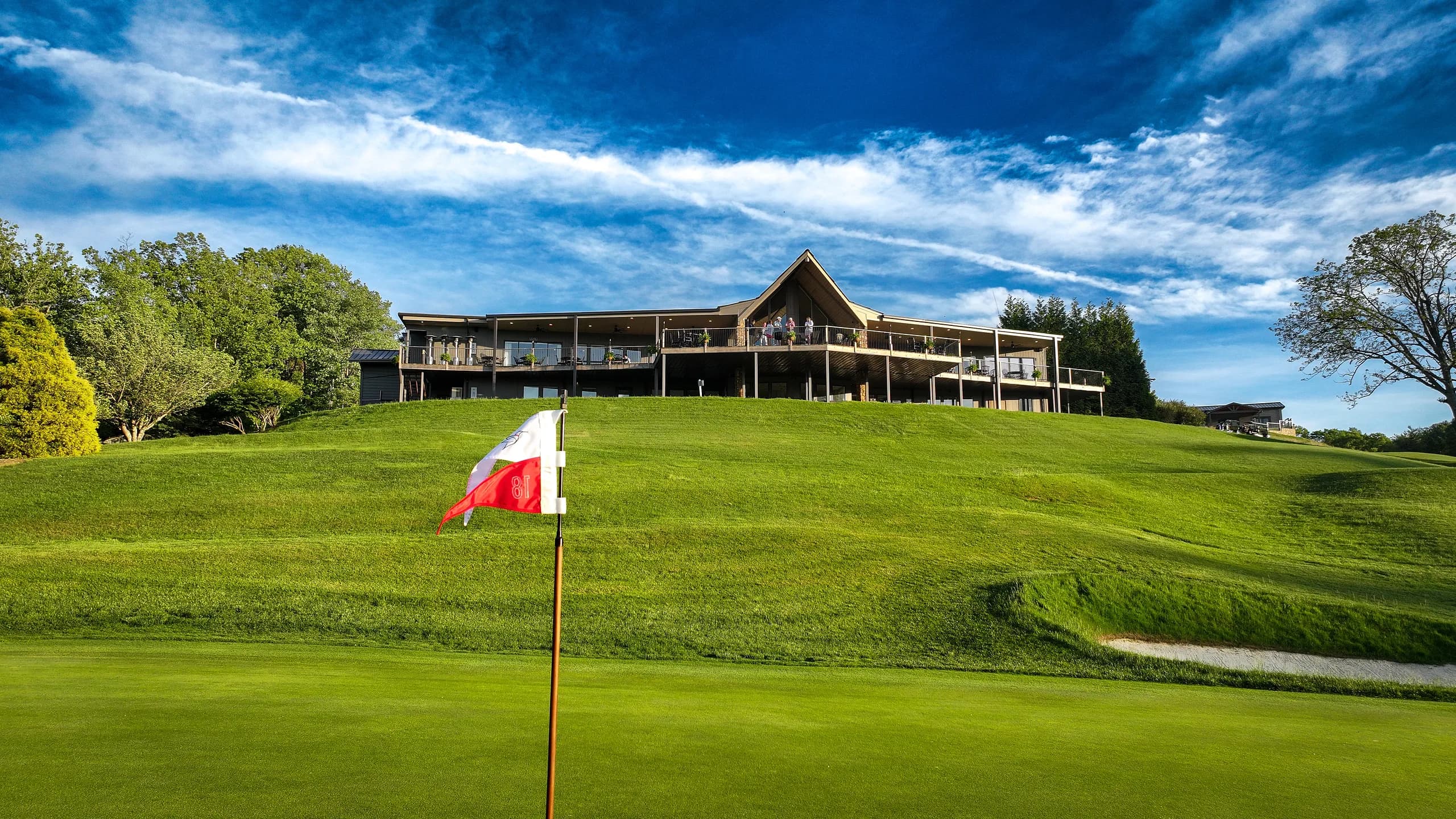 Pin flag on a green with the clubhouse on the hill behind, dramatic streaked sky