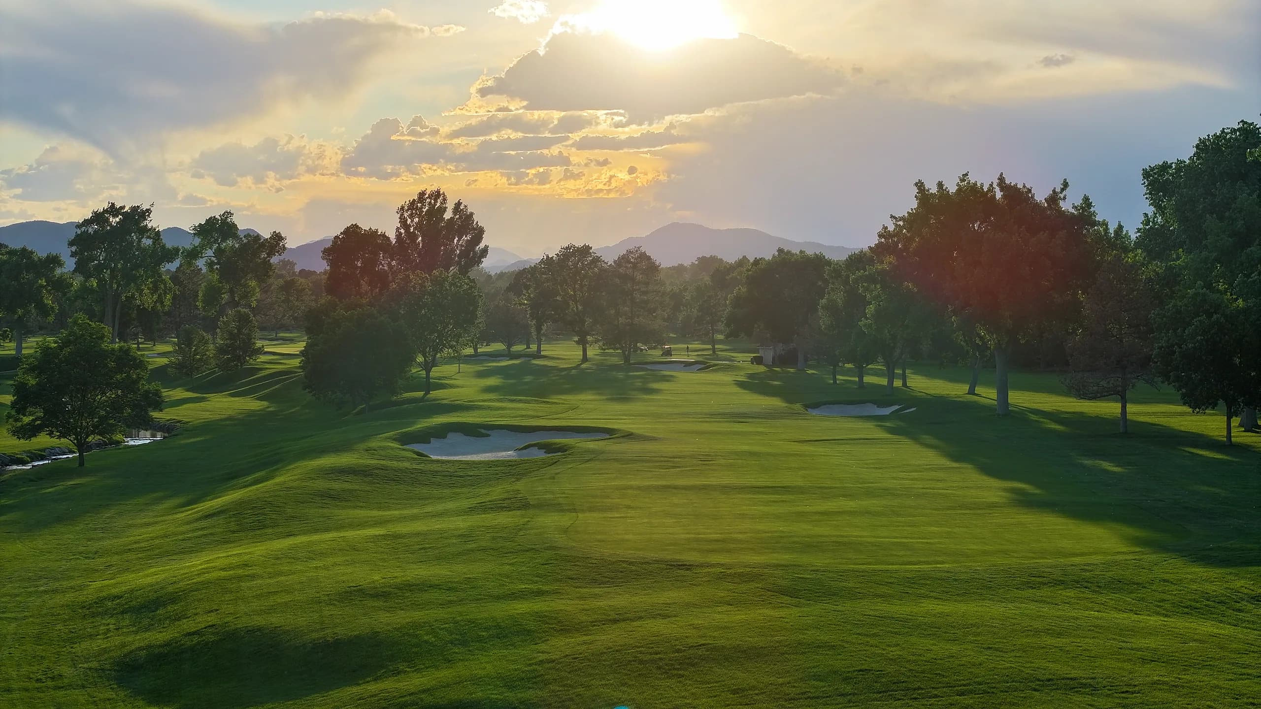 Sun breaking through clouds over a fairway with mountains on the horizon