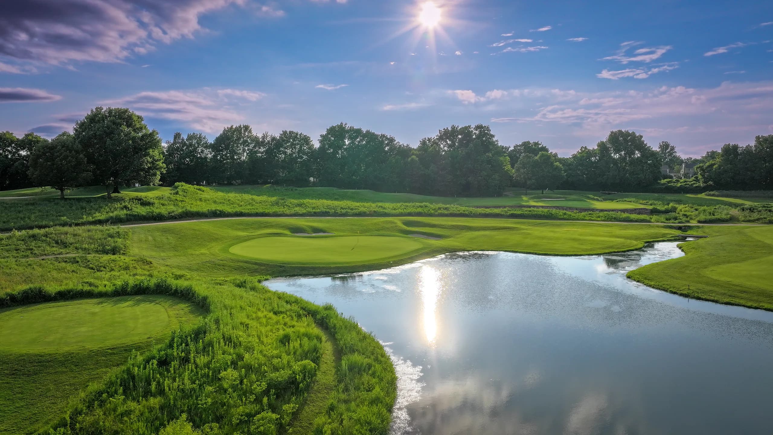 Evening sun reflecting off a wetland pond beside a mounded green