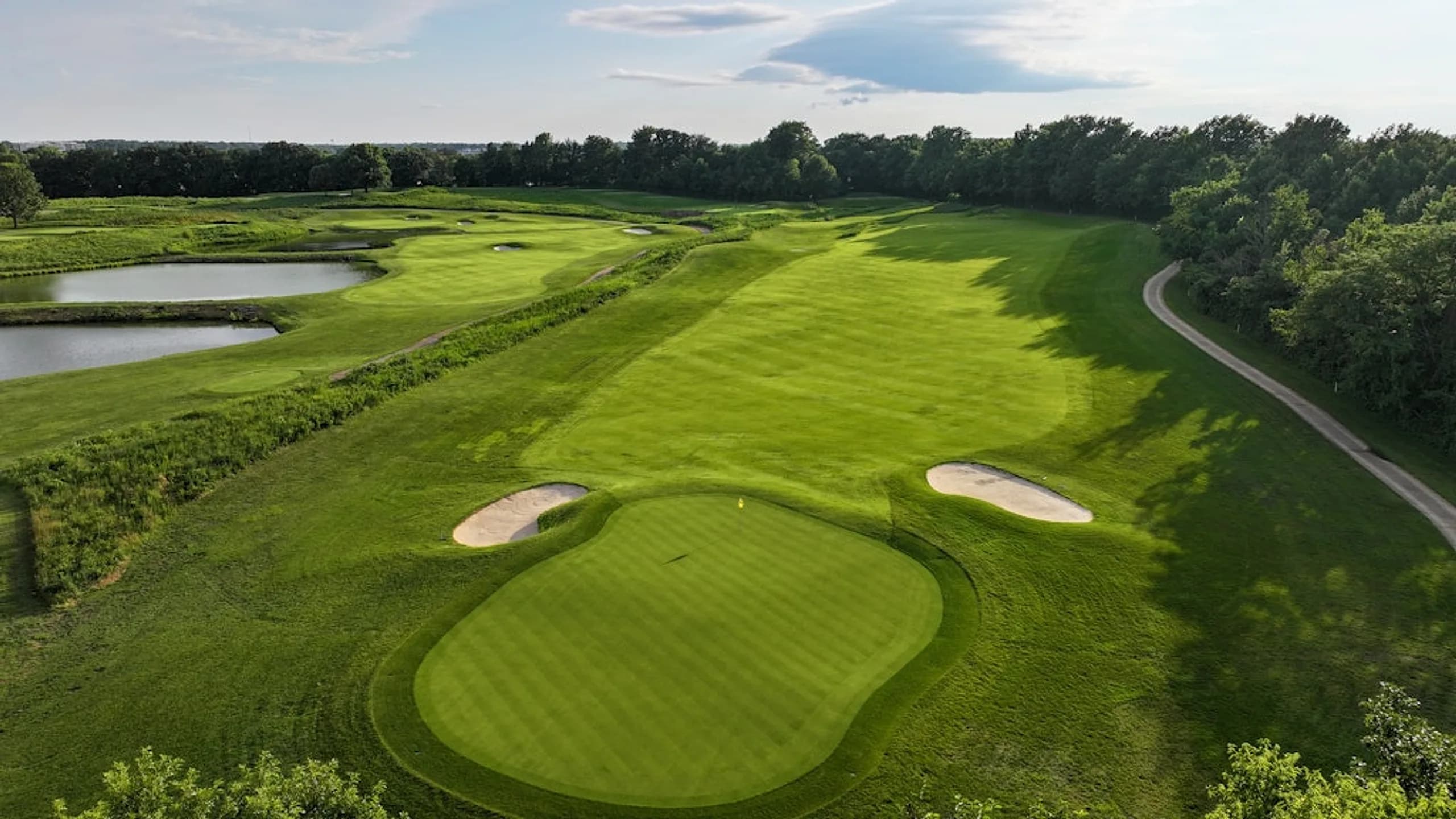 Long fairway running past wetland ponds to a bunkered green at a partner club