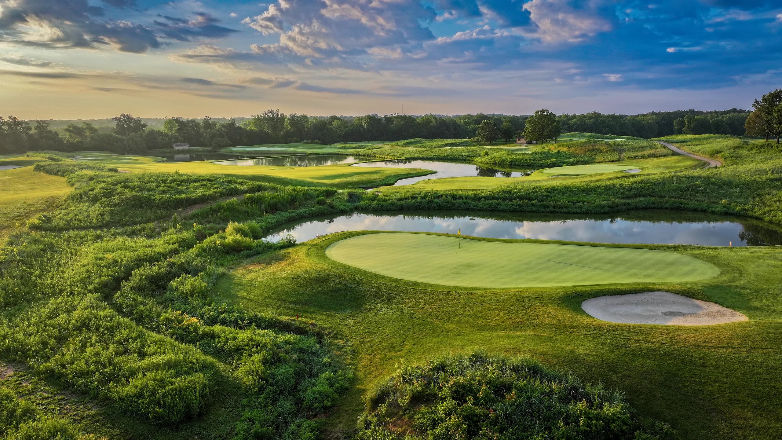 Dawn light across a wetland course with layered ponds and a bunkered green