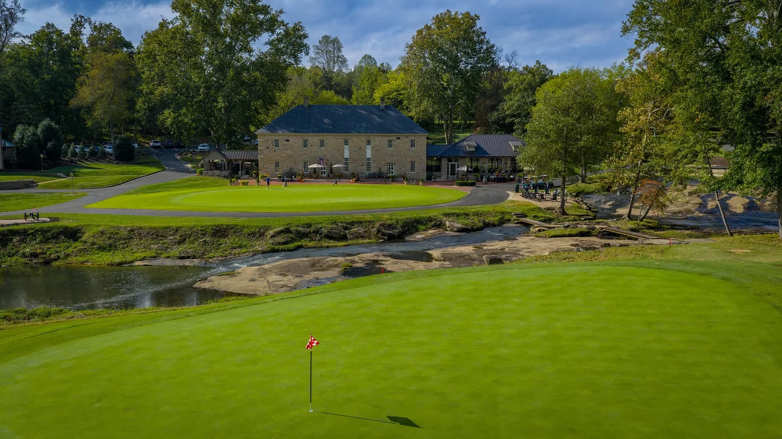 Historic stone clubhouse beside a green with a red pin flag