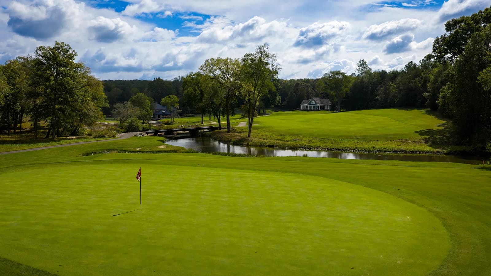 Green with a red flag beside a creek and stone bridge under big clouds