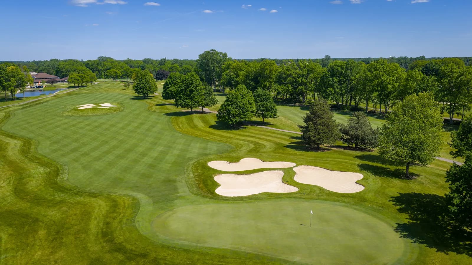 Striped fairway sweeping toward a green guarded by bunker clusters