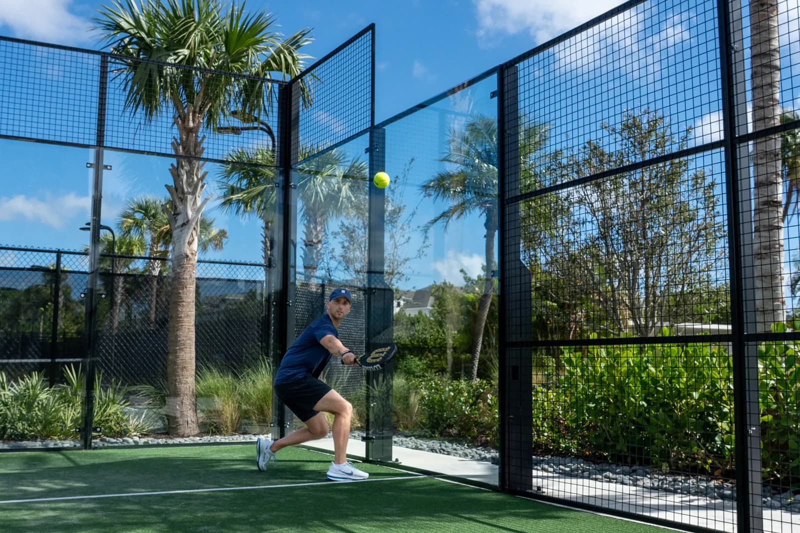 Padel player mid-swing inside the glass court at a partner club